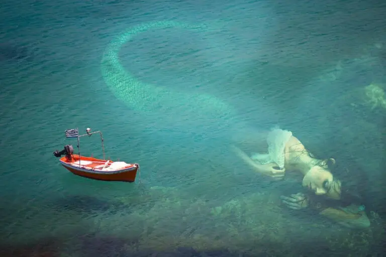 a giant mermaid under the surface of the ocean next to a boat
